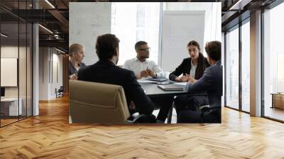 Diverse young and middle-aged partners engaged in group meeting, gathered in board room listen to team leader share ideas, offer solutions looks serious and confident. Business workshop event concept Wall mural