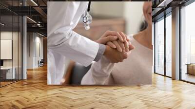 Doctor giving hope. Close up shot of young female physician leaning forward to smiling elderly lady patient holding her hand in palms. Woman caretaker in white coat supporting encouraging old person Wall mural