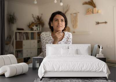 Dreamy thoughtful woman pondering research project, studying at home, standing at table with books and laptop, motivated young female student taking notes, writing essay, homework appointment Wall mural