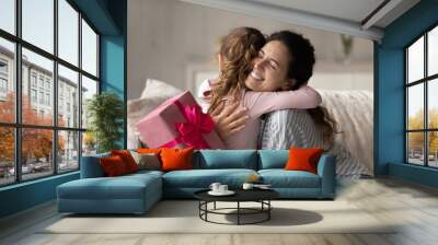 Emotional happy young mother feeling thankful getting surprise gift, cuddling little preschool kid daughter, celebrating birthday or special event together at home, joyful family sincere relations. Wall mural