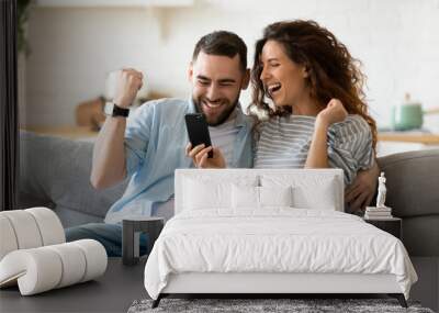 Excited couple holding smartphone celebrating online lottery win Wall mural