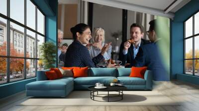 Excited diverse employees eating pizza during break in office together, happy Indian businesswoman laughing at funny joke, talking chatting with colleagues, having fun, sharing corporate lunch Wall mural