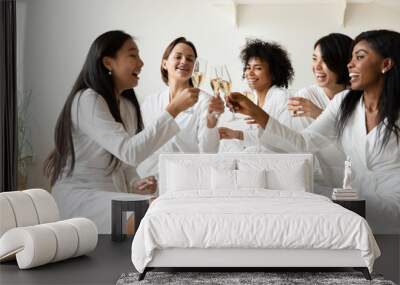 Excited diverse girls friends wear robes celebrating clinking champagne glasses Wall mural