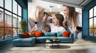 Excited little child girl holding brush puts powder on grandmas face doing make-up with mom and grandmother, happy kid granddaughter applying makeup on granny having fun in 3 generations women family Wall mural