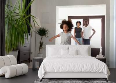 Excited little funny african girl running exploring big modern house moving in, happy black parents and kid daughter coming into new home, cute mixed race child having fun in hallway, family mortgage Wall mural