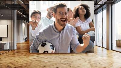 Excited man celebrating goal, watching football with diverse friends Wall mural