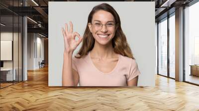 Excited satisfied young woman wearing glasses showing ok gesture Wall mural