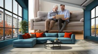 Father and grown up son sit together on sofa with computer Wall mural