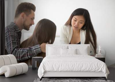 Female Asian broker show house plan to happy millennial couple deciding to buy first home together, spouses visiting realtor to purchase property, man and woman listening to real estate agent talking Wall mural