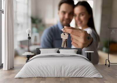 Focus on keys, held by excited young spouses homeowners. Happy married family couple celebrating moving in new house home , demonstrating keys, standing in apartment, real estate mortgage concept. Wall mural