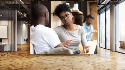 Focused African American woman talking with man in cafe, girlfriend discussing relationships with boyfriend, explaining, gesticulating, friends having serious conversation, sitting together on couch Wall mural