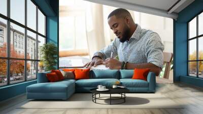 Focused african man student freelancer making notes studying with laptop Wall mural