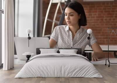 Focused asian business woman working looking at laptop making notes Wall mural