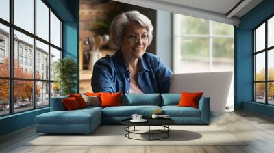 focused happy elderly 60s grey-haired woman in glasses look at laptop screen work online at home. sm Wall mural