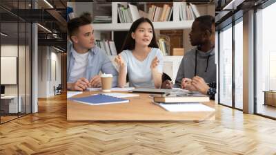 Focused international students sit at desk discuss school educational project brainstorm together, concentrated multiethnic young people study at shared table consider work on paperwork in classroom Wall mural