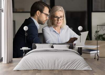 Focused senior business professional complaining on laptop, software work problem to application developer, computer expert, sitting at laptop, pointing at display, speaking Wall mural