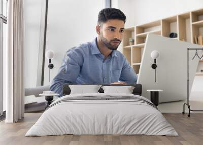 Focused serious young Arab employee man in casual typing on laptop, working in office, sitting at workplace table, browsing business social network, chatting on professional app, service Wall mural