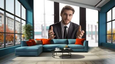 Focused young Caucasian male employee in suit look at camera talk on webcam conference with business partner, confident businessman speak on video call, engaged in online discussion or webinar Wall mural