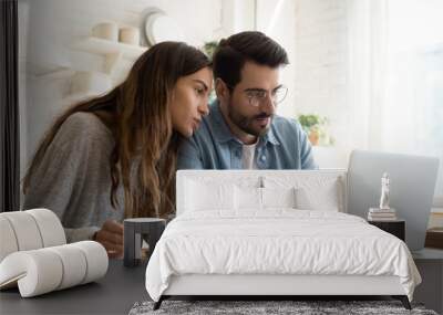 Focused young couple calculating bills, discussing planning budget together, serious wife and husband looking at laptop screen, using online banking services and calculator, checking finances Wall mural