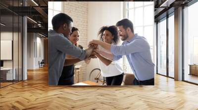 Four millennial different ethnicity teammates stacked palms together feels unity and support. Celebrating profitable deal, common success, leadership in market, participating in team building concept Wall mural