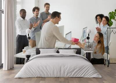 Friendly diverse corporate team congratulating happy female colleague with birthday and applauding, male employee presenting gift box greeting woman making pleasant surprise to coworker in office Wall mural