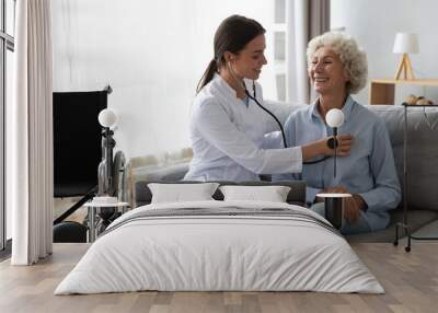 Friendly doctor listening to older woman lung or heart sound Wall mural