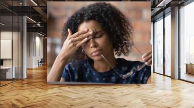 Frustrated black female freelancer overworked by computer feel headache migraine take off eyewear rub nose bridge. Exhausted tired young biracial lady suffer of eye pain vision problem chronic fatigue Wall mural