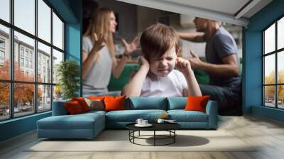 Frustrated kid son puts fingers in ears not listening to noisy parents arguing, stressed preschool boy suffering from mom and dad fighting shouting, family conflicts negative impact on child concept Wall mural