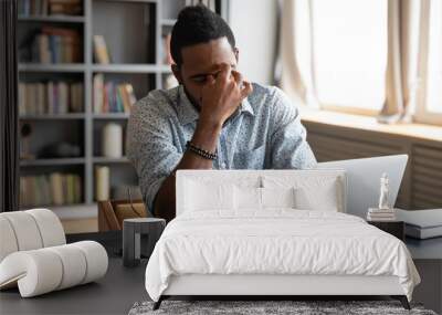 Frustrated young biracial guy taking off eyeglasses, massaging nose bridge, feeling tired due to computer overwork. Overwhelmed stressed millennial african american man suffering from eyes strain. Wall mural