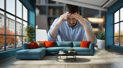 Frustrated young man in glasses sitting at table, feeling stressed calculating earnings or domestic expenses. Unhappy millennial guy suffering from lack of money, banking debt bankruptcy concept. Wall mural