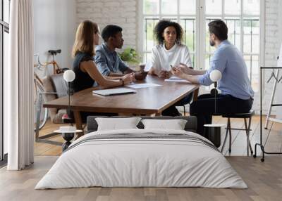 Full length motivated young mixed race business people sitting at table, creating project ideas, discussing problem solution, negotiating working issues or brainstorming at group office meeting. Wall mural