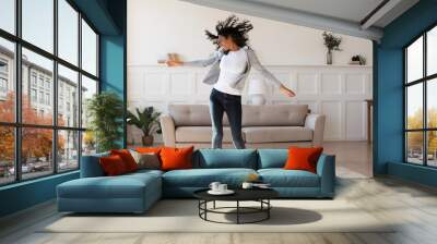 Full length young african ethnicity multiracial woman in casual wear dancing to favorite energetic audio music, having fun alone in living room, enjoying active domestic hobby pastime, feeling freedom Wall mural