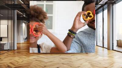 Funny African American dad and daughter girl making pepper slice glasses, having fun while cutting vegetables, cooking in kitchen together. Family eating at home, healthy food concept. Banner photo Wall mural