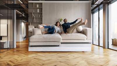 funny excited millennial spouses of new homeowners falling on big soft couch at home. young couple c Wall mural