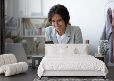 Good news. Excited young female self employed clothing designer sitting at work desk focused on mobile phone screen. Woman flower arranger reading email with profitable offer from potential customer Wall mural