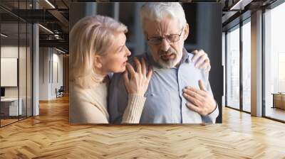 Grey haired man touching chest, having heart attack, woman supporting Wall mural