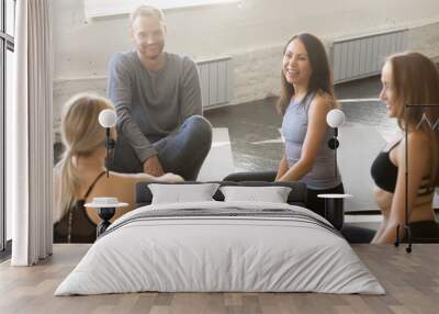 Group of fit happy people sitting on mats in fitness studio room chatting, joking, laughing together, talking in a circle after practice. Concepts of teamwork, mindfulness, active life benefits, break Wall mural