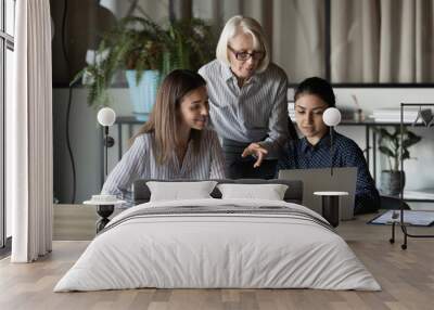 Group of two multiethnic females students sit at desk on workshop seminar listen to experienced mature woman teacher. Aged lady team leader boss explaining work to younger staff members subordinates Wall mural