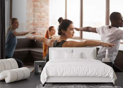 Group of young sporty people practicing yoga lesson standing in Warrior two exercise, Virabhadrasana 2 pose, working out, indoor close up, studio Wall mural