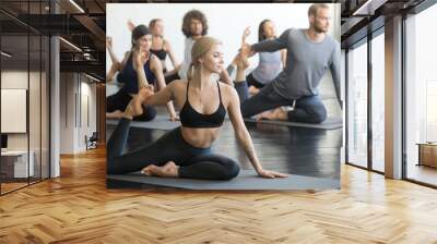 Group of young sporty people practicing yoga lesson with instructor, sitting in Mermaid exercise, Eka Pada Rajakapotasana pose, working out, indoor full length, students training in club, studio Wall mural