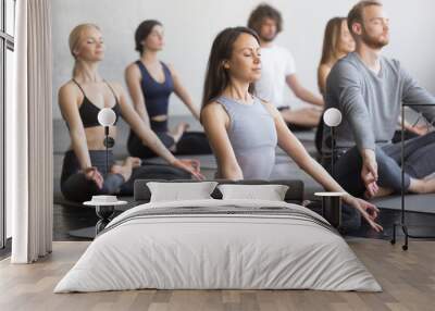 Group of young sporty people practicing yoga lesson with instructor, sitting in Padmasana exercise, Lotus pose, working out, indoor full length, students training in club, studio Wall mural