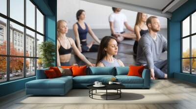 Group of young sporty people practicing yoga lesson with instructor, sitting in Padmasana exercise, meditating with closed eyes, Lotus pose, working out, indoor, students training in club, studio Wall mural