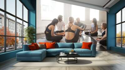 Group of young sporty people relaxing sitting in circle after workout. Enjoy pleasant effective communication, allowing body to recover to avoid overworking in gym, indoor studio. Wellbeing concept Wall mural