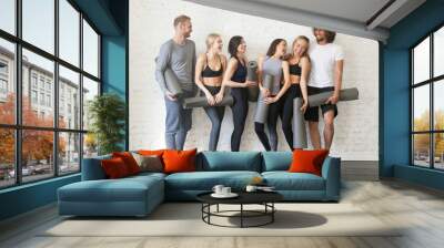 Group portrait of young sporty excited people with exercise mats standing beside white wall joking and laughing together. Candid funny students taking rest from fitness activity. Full length photo Wall mural