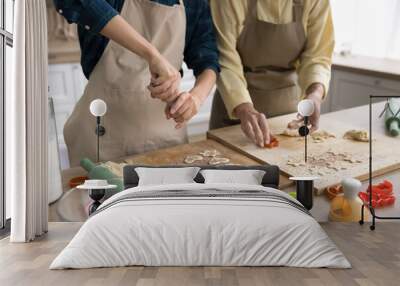 Hands of two younger and older baker women in kitchen aprons cutting fresh dough for cookies on table, baking heart and star shaped biscuits together, preparing homemade sweet Wall mural