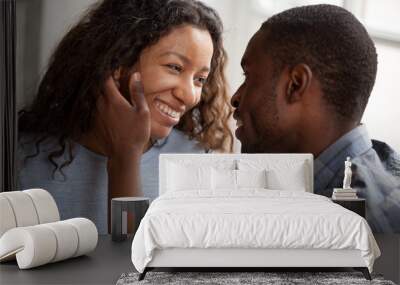 Happy African American couple having date at home, sitting together on couch, loving man touching attractive smiling woman face with tenderness, looking in eyes to each other, feelings, first kiss Wall mural