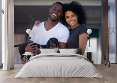 Happy african american millennial couple embrace outdoors holding dachshund, smiling young black man woman enjoying time outside house having fun with dog looking at camera, family and pet portrait Wall mural