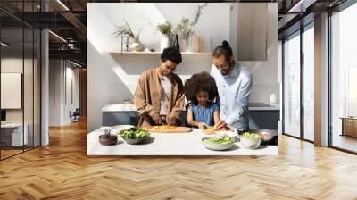 Happy African family couple teaching sweet daughter kid to cook healthy vegetarian dinner, chopping fresh vegetables for salad. Kin helping parents to prepare lunch at kitchen table Wall mural