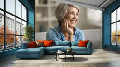 Happy beautiful blonde older mature lady touching facial skin, looking away with perfect toothy smile, laughing, enjoying elderly beauty care, thinking on good skincare result Wall mural