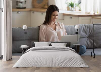 Happy beautiful woman using laptop relaxing with technology on couch Wall mural